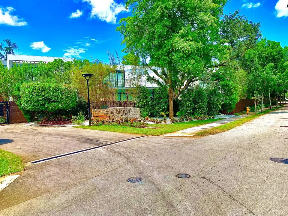 Street-side entrance with defined lawn edges, white stone planting beds, and mature trees after the landscape update